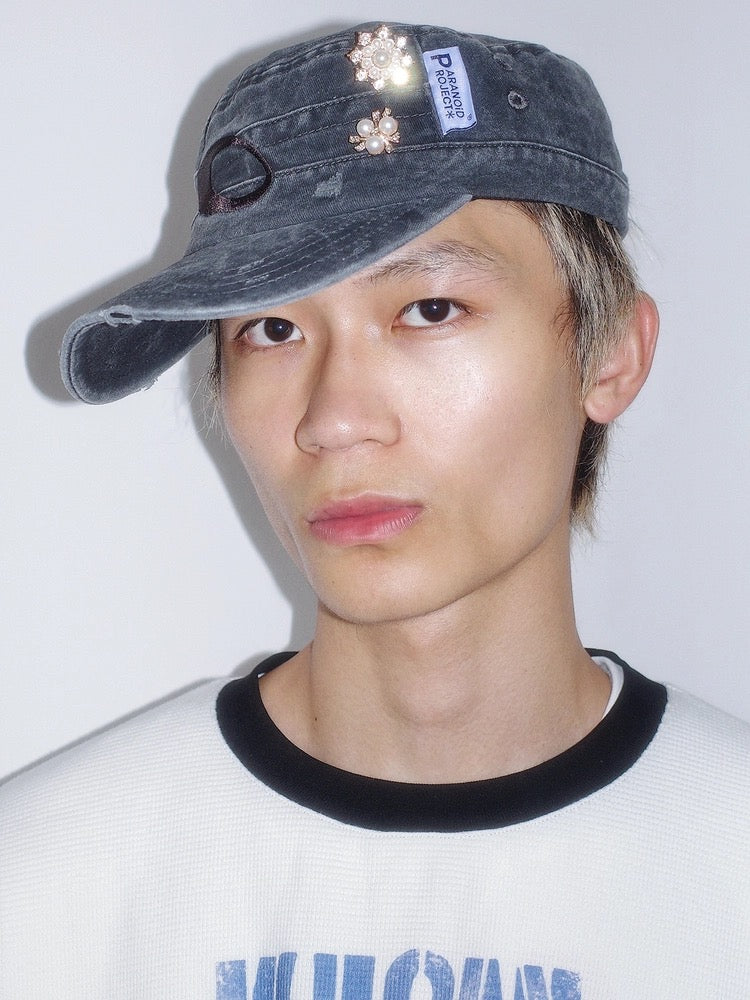 Person wearing a denim cap with decorative elements on a plain background