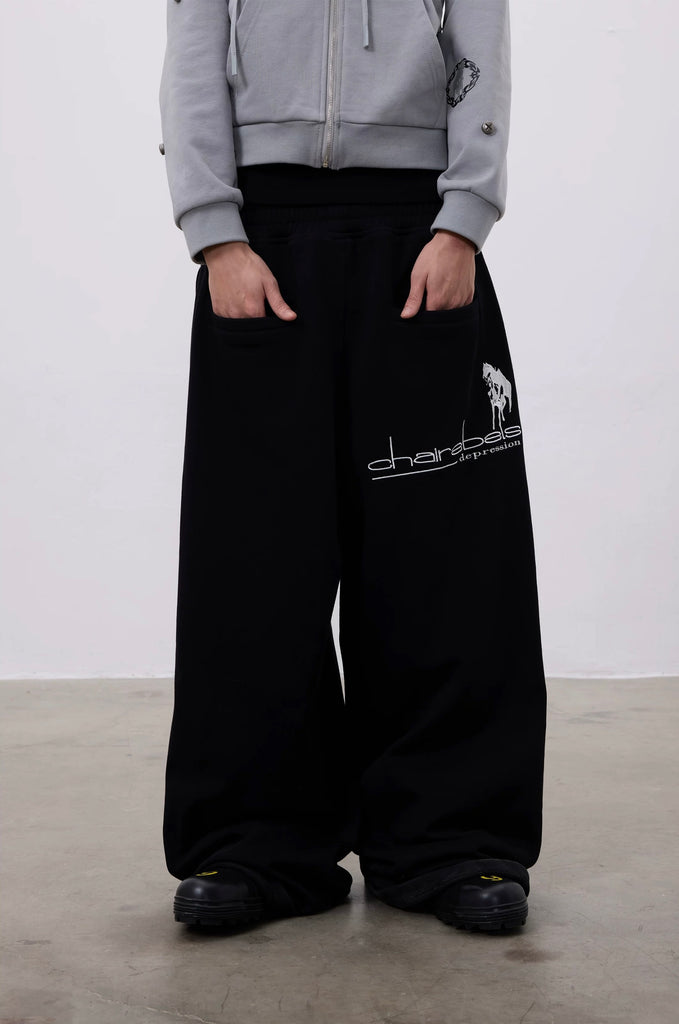 Person wearing black wide-leg pants with a logo and gray hoodie on a plain background