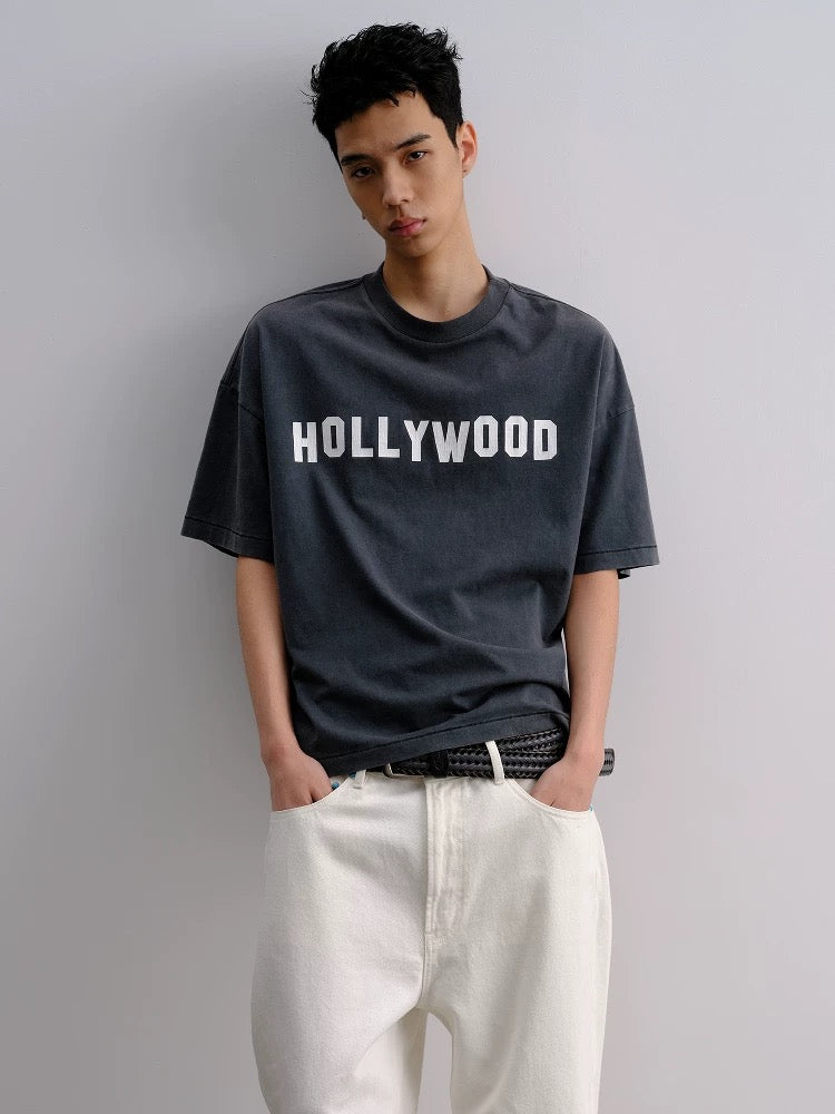 Person wearing a black t-shirt with 'HOLLYWOOD' text on a plain background