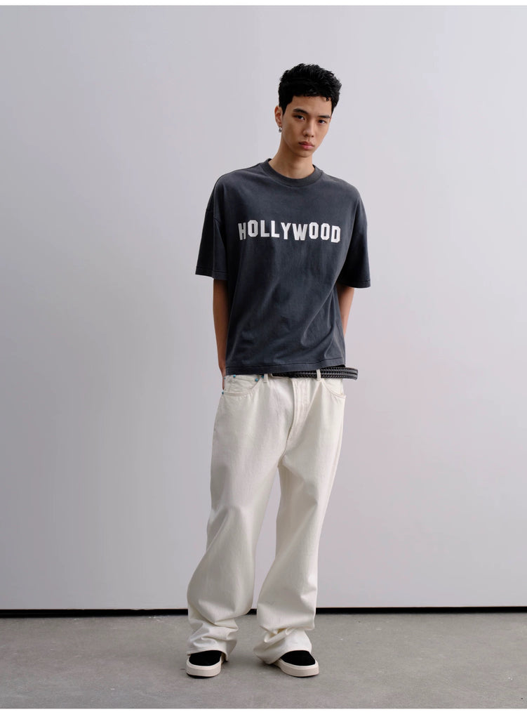 Person wearing a black 'HOLLYWOOD' t-shirt and white pants against a plain background